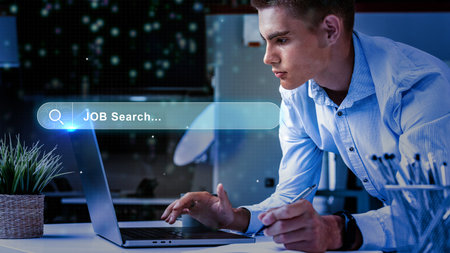 Young professional engaged in online job search at modern workspace during evening hoursの写真素材