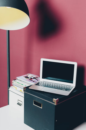 Different stationery at home office of a woman with laptop against dark pink wall