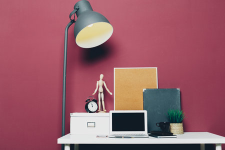 Different stationery at home office with laptop against dark pink wall