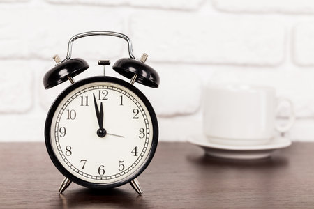 Alarm clock on brown wooden table and coffee cup