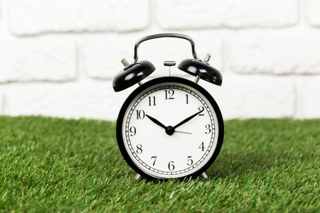 Black alarm clock on green grass front view