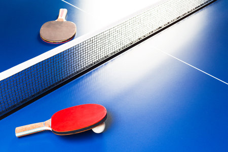 Two ping pong rackets and ball on blue table