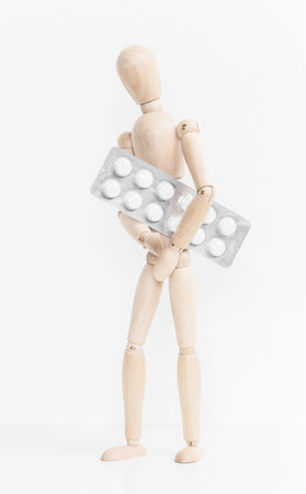 Wooden mannequin holds a blister pack of tablets against a white background