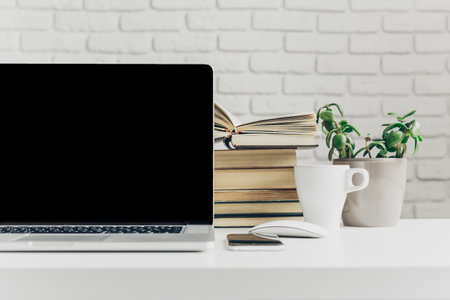 Workspace with a laptop, books, and plants in a modern settingの写真素材