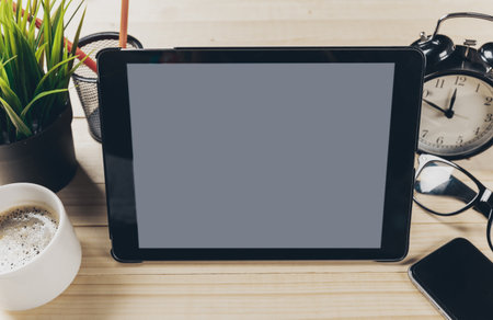 Workspace with tablet, clock, and plant on wooden desk in casual setting