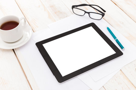 Workspace setup with tablet, coffee, and stationery on wooden table in a bright environment