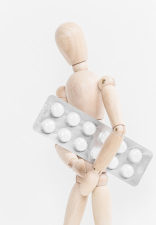 Wooden figure holds blister pack of pills against white background in simple composition