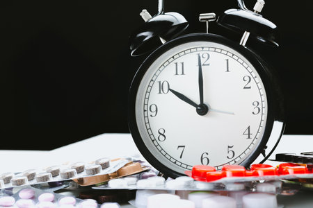 Clock and assorted pills on a table, symbolizing time management and medicationの写真素材