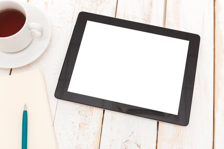 Tablet on wooden table next to coffee cup and notebook in a cozy workspace