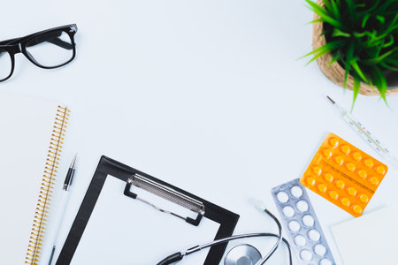 Medical workspace with clipboard, pens, glasses, and medications on a clean deskの写真素材