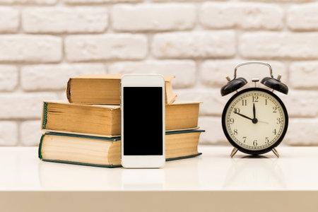 Old books and modern technology on a table with an alarm clock in a cozy setting