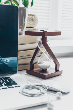 Modern workspace featuring a wooden hourglass and laptop with notebooks nearby
