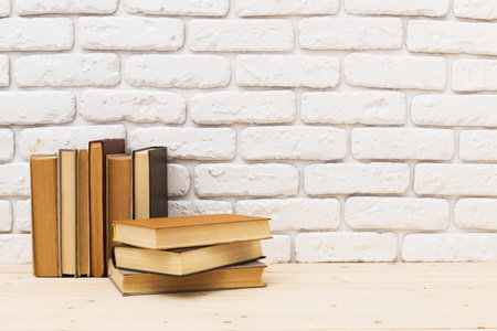 Stacked books resting on a table against a white brick wall background in a cozy settingの写真素材