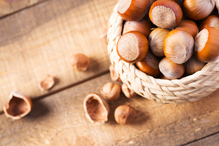 Freshly harvested hazelnuts in a woven basket on a rustic wooden surfaceの写真素材