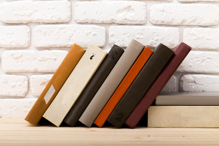 Collection of vintage books arranged neatly on a wooden shelf against a white brick wall