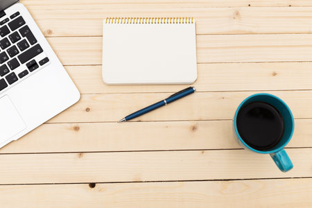 Workspace with laptop, notebook, pen, and coffee cup on wooden table during daytime