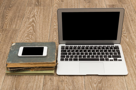 Digital workspace with laptop and smartphone on stack of old books in a cozy setting