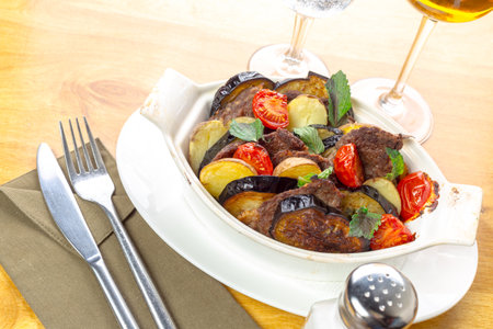 Delicious meat and vegetable dish served in a rustic white cookware on wooden tableの写真素材
