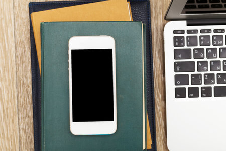 Desk setup featuring a smartphone on a stack of notebooks near a laptop
