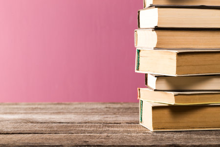 Stacked books on a rustic wooden table against a colorful backgroundの写真素材