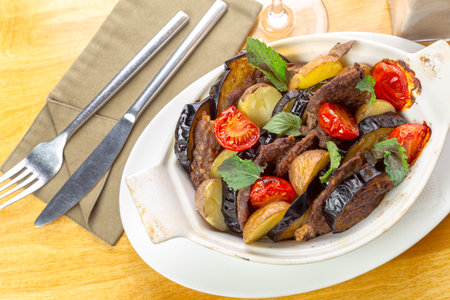 Delicious roasted meat with vegetables served in a ceramic dish at a restaurantの写真素材