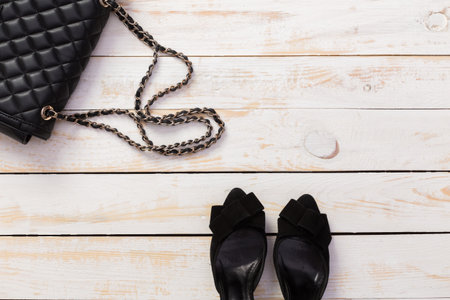 Stylish black handbag and elegant heels on a light wooden surfaceの写真素材