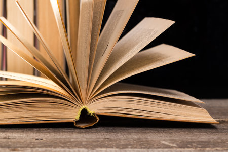 Open book resting on wooden table with pages fanned out towards the viewer in dim light
