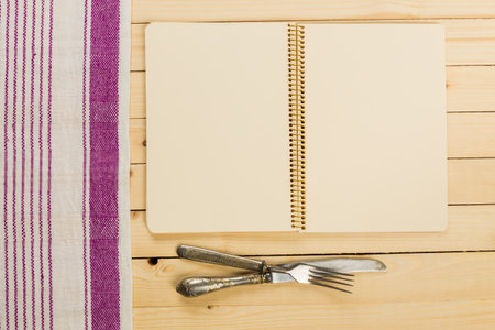 Blank notebook and silver cutlery on wooden table with clothの写真素材