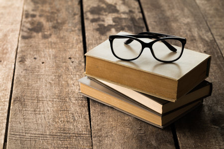 Glasses resting on a stack of vintage books on a rustic wooden surface