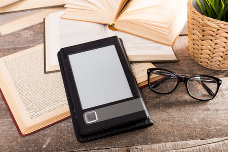 E-reader placed on a wooden table surrounded by books and glasses in a cozy reading environment