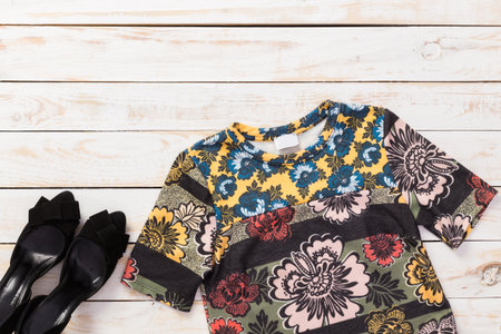 Stylish floral top and black heels arranged on a wooden surface for a fashion layout
