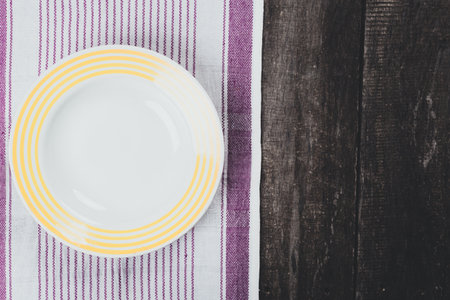 Simple white plate with yellow stripes on a textured wooden tableの写真素材