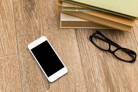 Smartphone, books, and glasses on wooden floor with soft lighting in a cozy study areaの写真素材