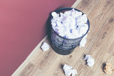 Crumpled paper fills a wastebasket in a home office setting during the afternoonの写真素材