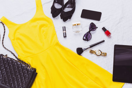 Fashion accessories arranged around a vibrant yellow dress on a white backgroundの写真素材
