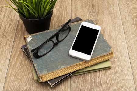 Reading materials and a phone arranged on a wooden surface with a plant nearbyの写真素材