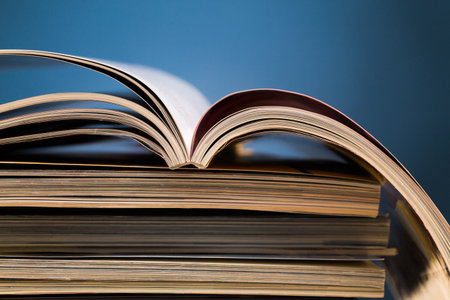 Open book resting on a stack of books against a blue backgroundの写真素材