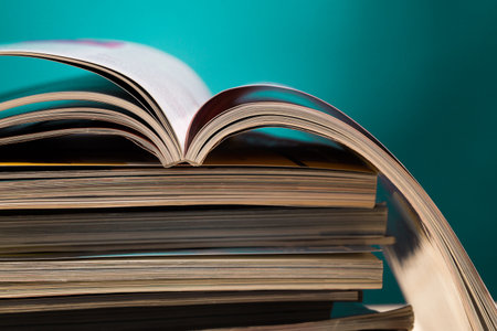 Stack of open magazines resting on top of closed ones against a vibrant backgroundの写真素材