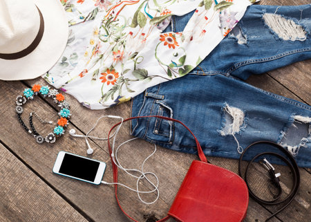 Stylish summer outfit flat lay featuring floral shirt, jeans, accessories, and smartphone