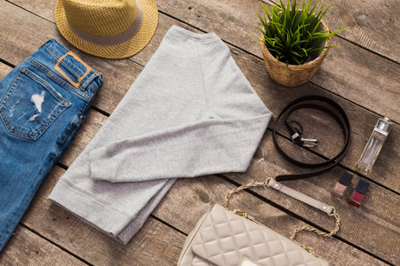 Outfit flat lay featuring denim jeans, gray sweatshirt, and summer accessories on wooden surfaceの写真素材
