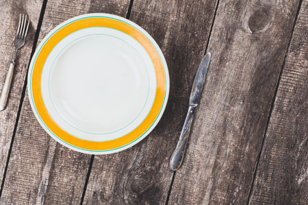 Empty plate with knife and fork on rustic wooden table ready for a meal