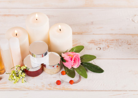 Relaxing spa setup with candles, cosmetic jars, and fresh flowers on a wooden tableの写真素材