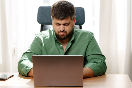 Focused man working on laptop in a well-lit home office