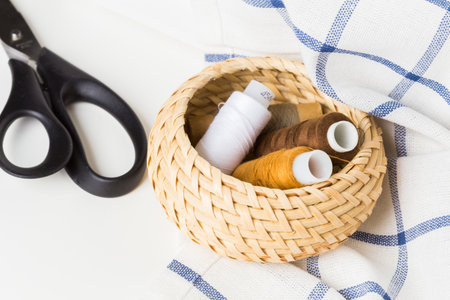 Sewing supplies arranged in a woven basket with scissors on a fabric