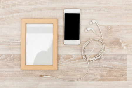 Smartphone and earphones beside a wooden picture frame on a light wooden surfaceの写真素材