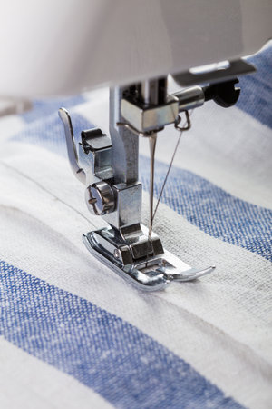 Close-up view of sewing machine needle working on striped fabric during daylight