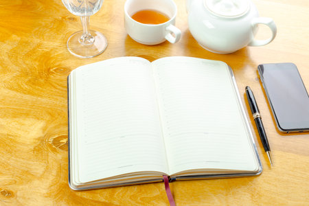 Open notebook on a wooden table with tea, glass, and smartphone in a cozy setting