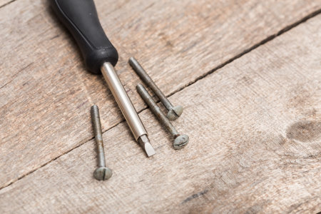 Tools on a wooden surface with screws and a screwdriver ready for repair tasksの写真素材