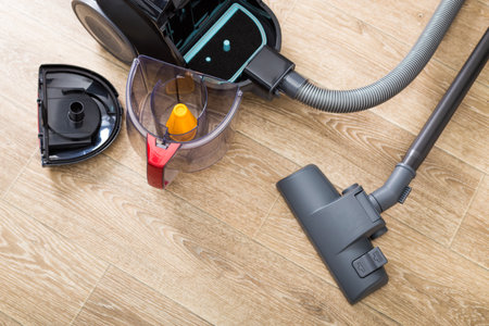 Cleaning process with a vacuum cleaner and dust canister on wooden floor surface