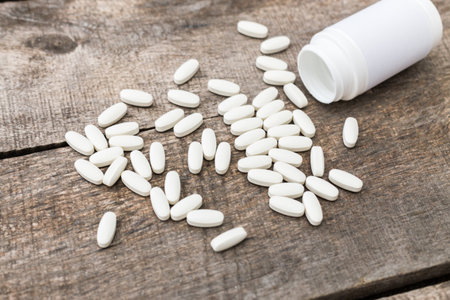 Pills spilled from a white bottle on a rustic wooden surface